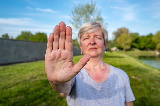 An senior woman shows a stop sign with her hand in nature