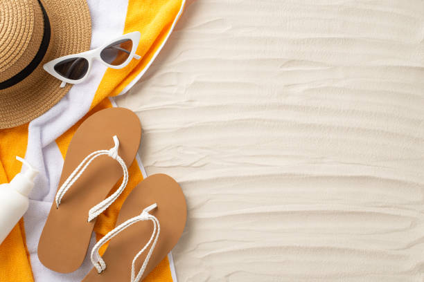 istock Soak up the sun's rays. Accessories laid out from top view: sunglasses, straw hat, flip-flops, sunscreen bottle, yellow towel. Sandy beach scene with an empty space for text or promotion 1496177452