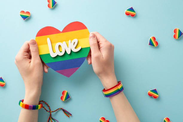 istock Show your support for the LGBT community with this inspiring image featuring a rainbow heart-shaped card held by woman's hands wearing a symbolic bracelets over pin badges on pastel blue background 1496177918