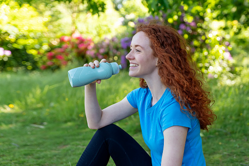 Happy  Woman Resting and drinking water After Exercising In Park. Fitness, sport and exercise concept
