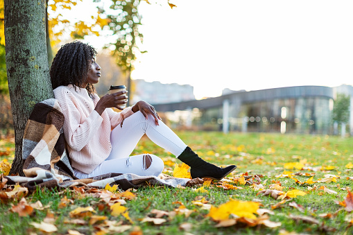 Black woman drinking coffee at park and relaxing