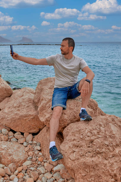 istock A man takes a selfie while sitting on large stones by the sea 1496186726