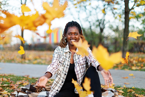 Young adult Black female throwing maple leaves in park