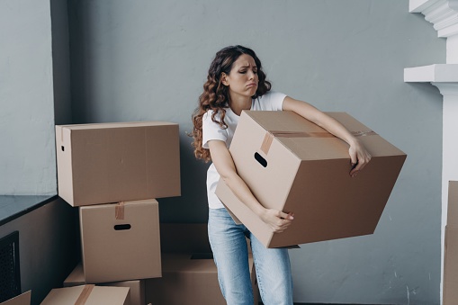 Exhausted renter carrying heavy boxes on moving day. Upset hispanic girl leaving rented apartment