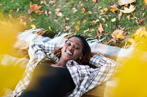 Young adult Black female lying down on picnic blanket at autumn park