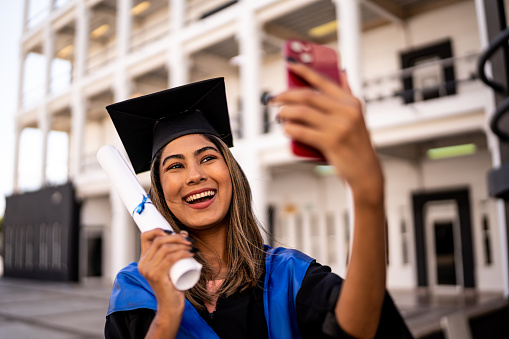 Young woman taking a selfie with her diploma on the graduation