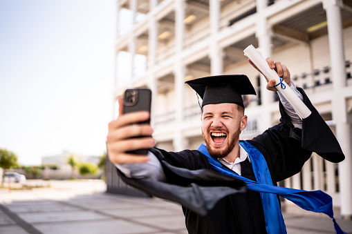 Young man taking a selfie with his diploma on the graduation
