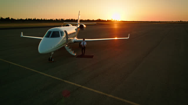 Shot Of Pilot Standing Next To Private Jet At Sunset
