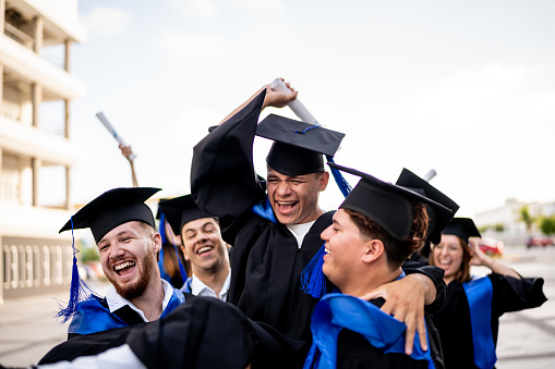 Young man being thrown up by his friends while celebrating on graduacion