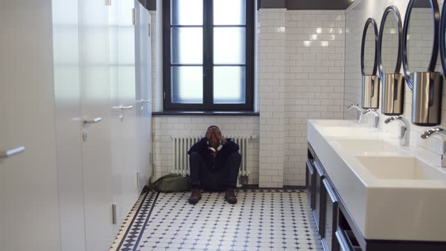 Upset African-American teen student sit on floor in school bathroom