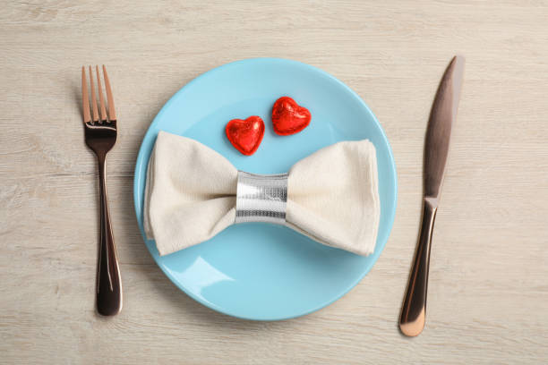 Beautiful table setting with heart shaped candies for romantic dinner on white wooden table, flat lay