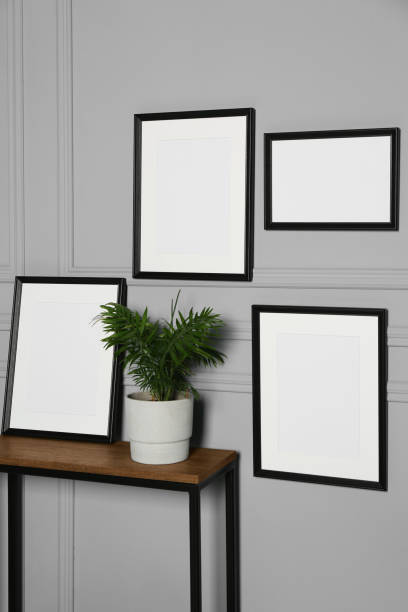 istock Empty frames hanging on grey wall near wooden table indoors 1496197419
