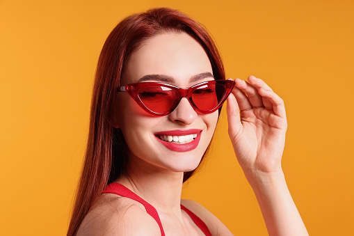 Happy woman with red dyed hair and sunglasses on orange background