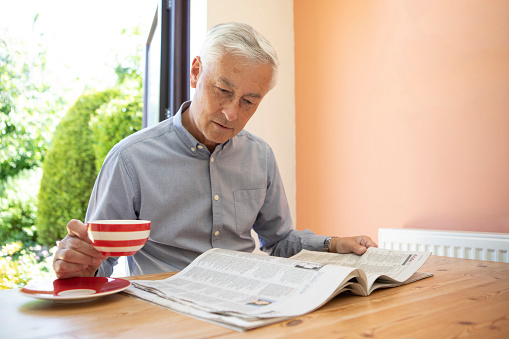 Mature adult male sitting at a table with a newspaper in a bright room at home