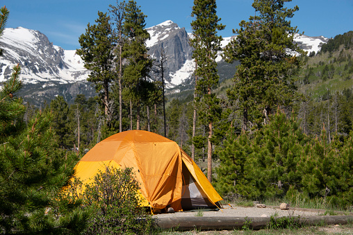 Tenting in orange tent camping with Hallet Peak and snow covered Rocky Mountains of Colorado, USA
