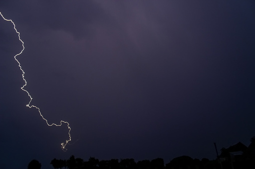 Rainy sky on a summer night with a flash of lightning on the left side of the sky, with the roofs of rural buildings.