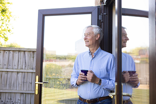 Mature man standing by patio doors and looking out onto his back garden