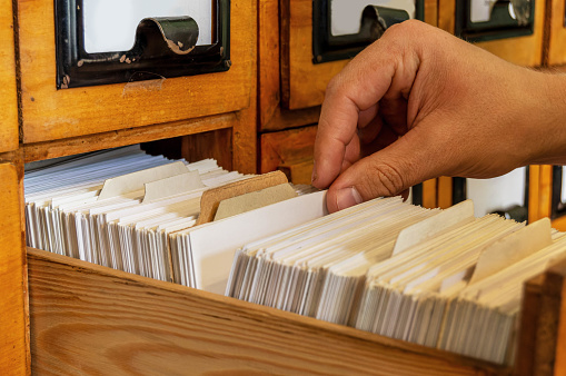 A man looks through cards in an old open wooden file cabinet with his hand. Sorting, library, retro