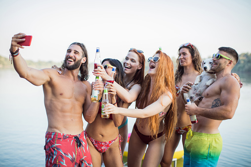 Group of friends dancing at party on deck. They are happy and joyful. Wearing swimsuits and making selfie