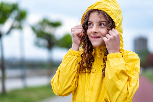a little girl happily watches the rain fall in a raincoat