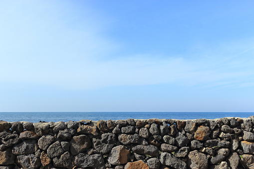 The blue sky that touches the horizon of the blue sea seen over the stone wall in Jeju Island