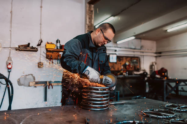 istock Locksmith in special clothes and goggles works in production. Metal processing with angle grinder. Sparks in metalworking. 1496215648