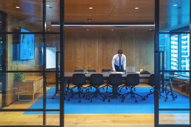 istock Business man standing and working in an office leaning on a conference table. He is standing in behind a board room table 1496219530