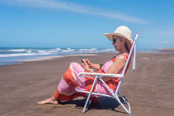 istock Mature woman using a mobile phone while relaxing at the beach. 1496220671