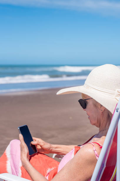 Relaxed mature woman using a mobile phone at the beach.