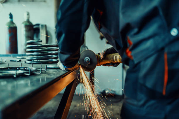 istock Locksmith in special clothes and goggles works in production. Metal processing with angle grinder. Sparks in metalworking. 1496221165
