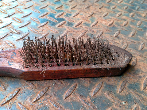 Old used Steel wire brush tool on a corroded iron textured background. Tooling tools to clean metal from corrosion