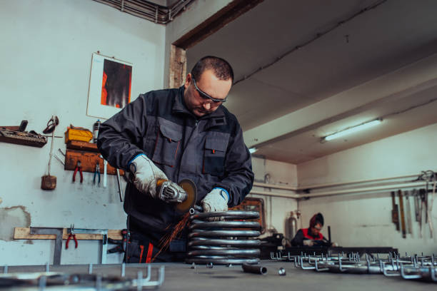 istock Locksmith in special clothes and goggles works in production. Metal processing with angle grinder. Sparks in metalworking. 1496222229