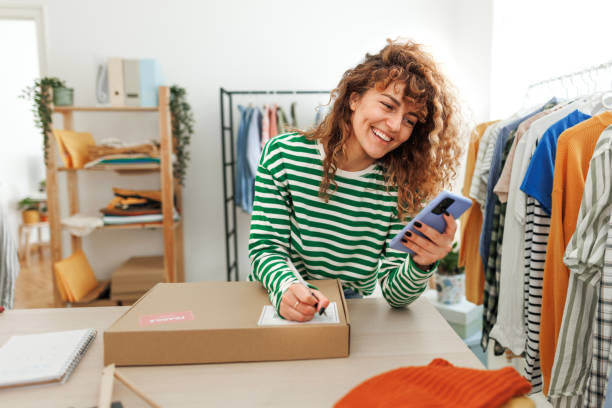 istock Young beautiful smiling woman using smart phone at her home based clothing store 1496223992