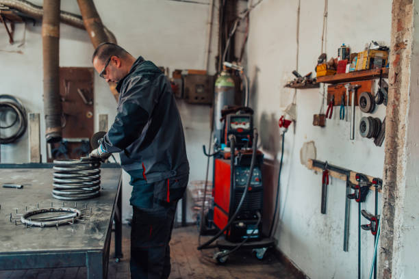 istock Locksmith in special clothes and goggles works in production. Metal processing with angle grinder. Sparks in metalworking. 1496225843
