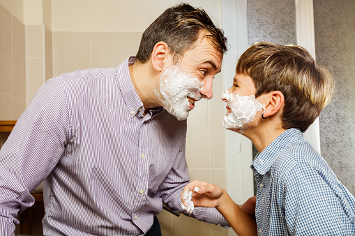 Father and son with shaving foam on the face play together touching foreheads, smiling