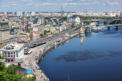 Cityscape overlooking the embankment from the right bank of the Dnipro in Kyiv, the area of the river station and Podil with a number of bridges across the river on a sunny summer day. Bird's-eye view. 06.04.2023. Kyiv. Ukraine.