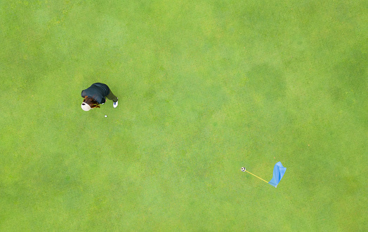 A high angle direct above view of a female golfer making a put on a golf green.
