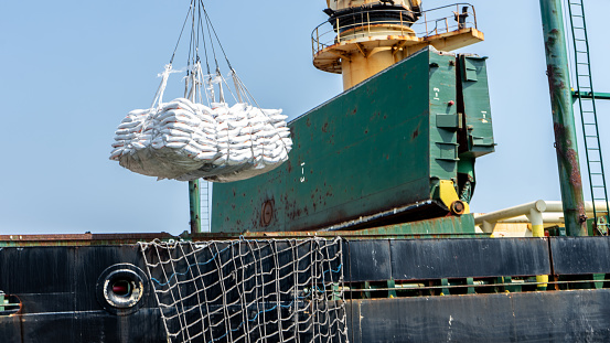 Industrial crane loading sacks of raw material to an international ship for export and import