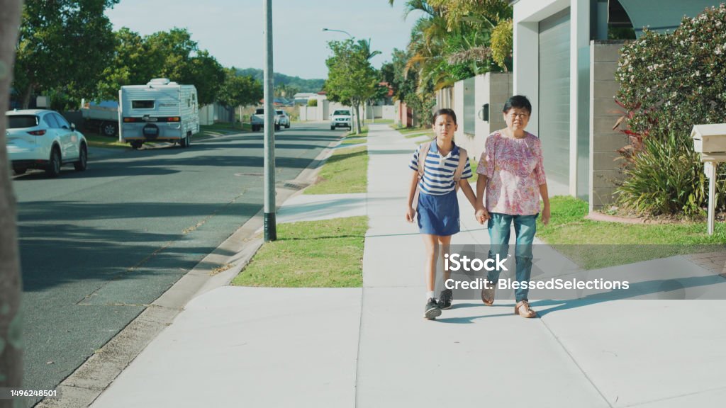 Asian senior woman walking her primary school student granddaughter to school on sunny day, active travel, healthy lifestyle Family Stock Photo