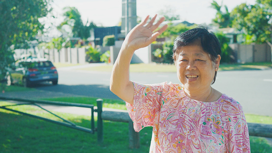 Asian senior woman waving goodbye to her primary school student granddaughter front of school, active travel, healthy lifestyle