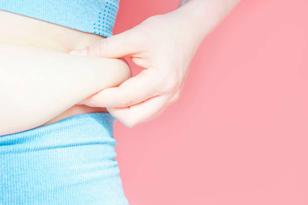 Female hand holding excessive belly fat on pink background, overweight concept. stock photo