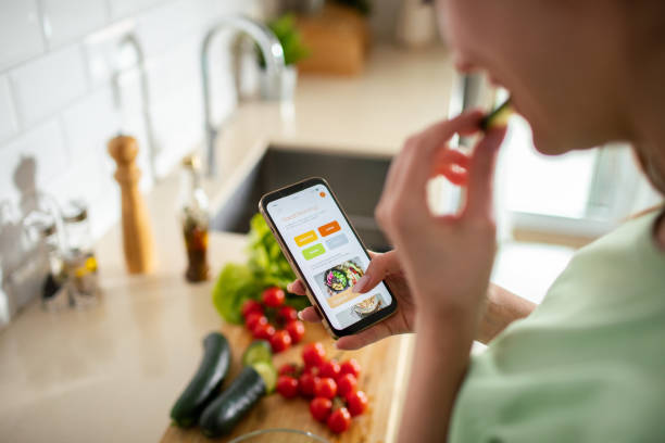 istock Young woman using a diet app on her phone while preparing a healthy food dish at home 1496267849