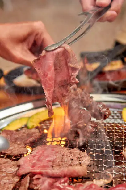 Photo of Hands holding tongs to grill meat on the stove, yakiniku buffet. popular food.