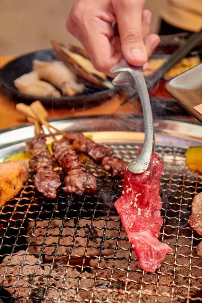 Photo of Hands holding tongs to grill meat on the stove, yakiniku buffet. popular food.