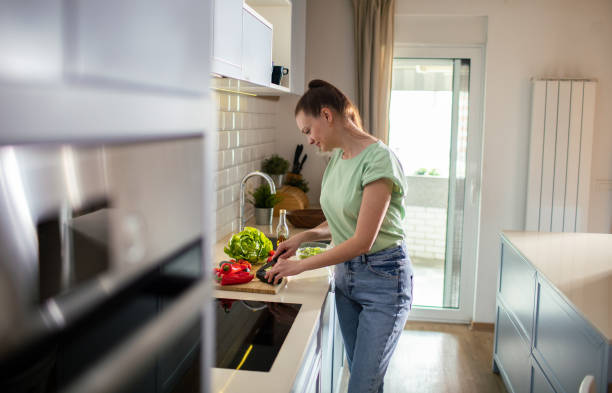 istock Young woman cutting and preparing vegetables in a kitchen at home 1496268774