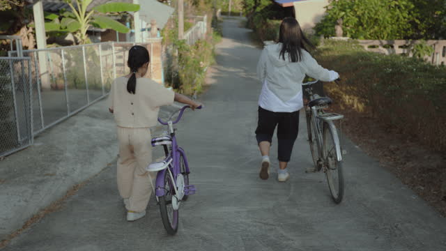 Mother and daughter leading a bicycle leave from home together