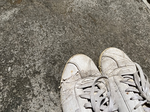 Pair of dirty and worn out white sneakers on concrete background from top view.