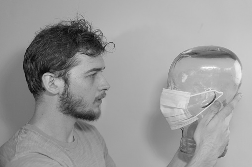 Man holding up a mannequin head made of glass with a face mask over it