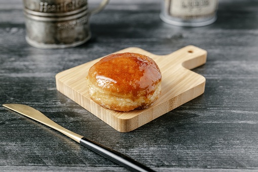 A wooden cutting board with a freshly baked donut with a kitchen knife beside it