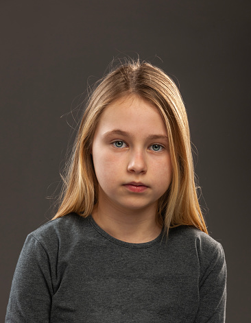 Studio Portrait of a young girl with blue eyes and blond hair. Looking sad, serious.